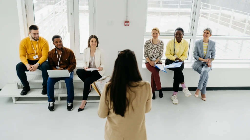 A woman speaks to a group of attentive listeners in a well-lit room, engaging them with her presentation.