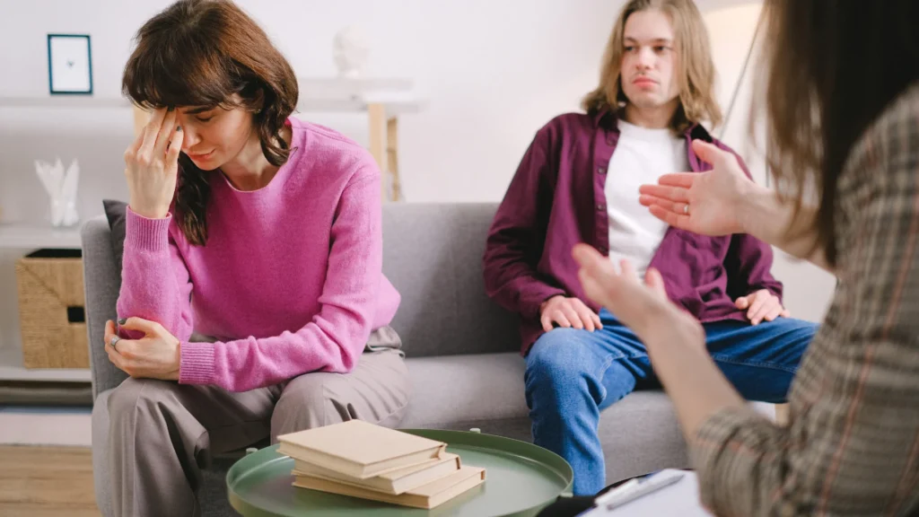 A woman converses with a man and another woman seated on a couch in a cozy living room setting.